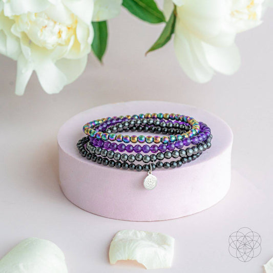 Stacked beaded bracelet set with purple, black, and rainbow beads plus silver charm