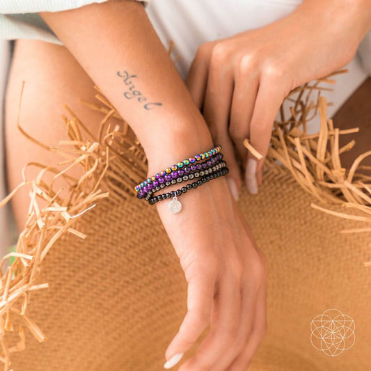 Beaded bracelet set on wrist with purple and black rows and round silver charm