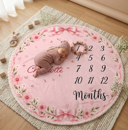 Round pink milestone blanket on rug with baby lying on it, floral border and Charlotte