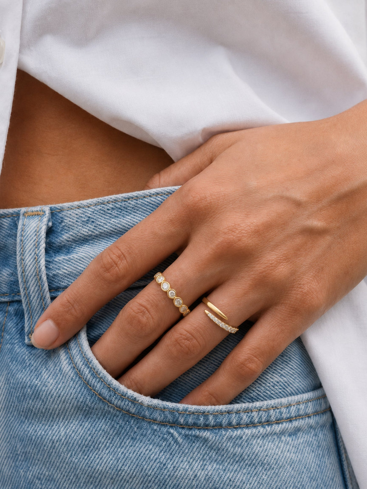 Gold spiral ring with pave white stones, alongside a plain gold ring on finger