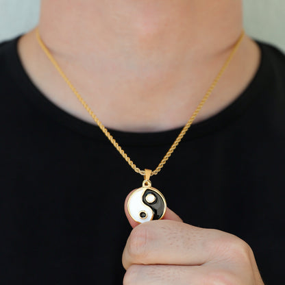 Gold yin yang pendant necklace held by hand; black and white enamel yin-yang charm